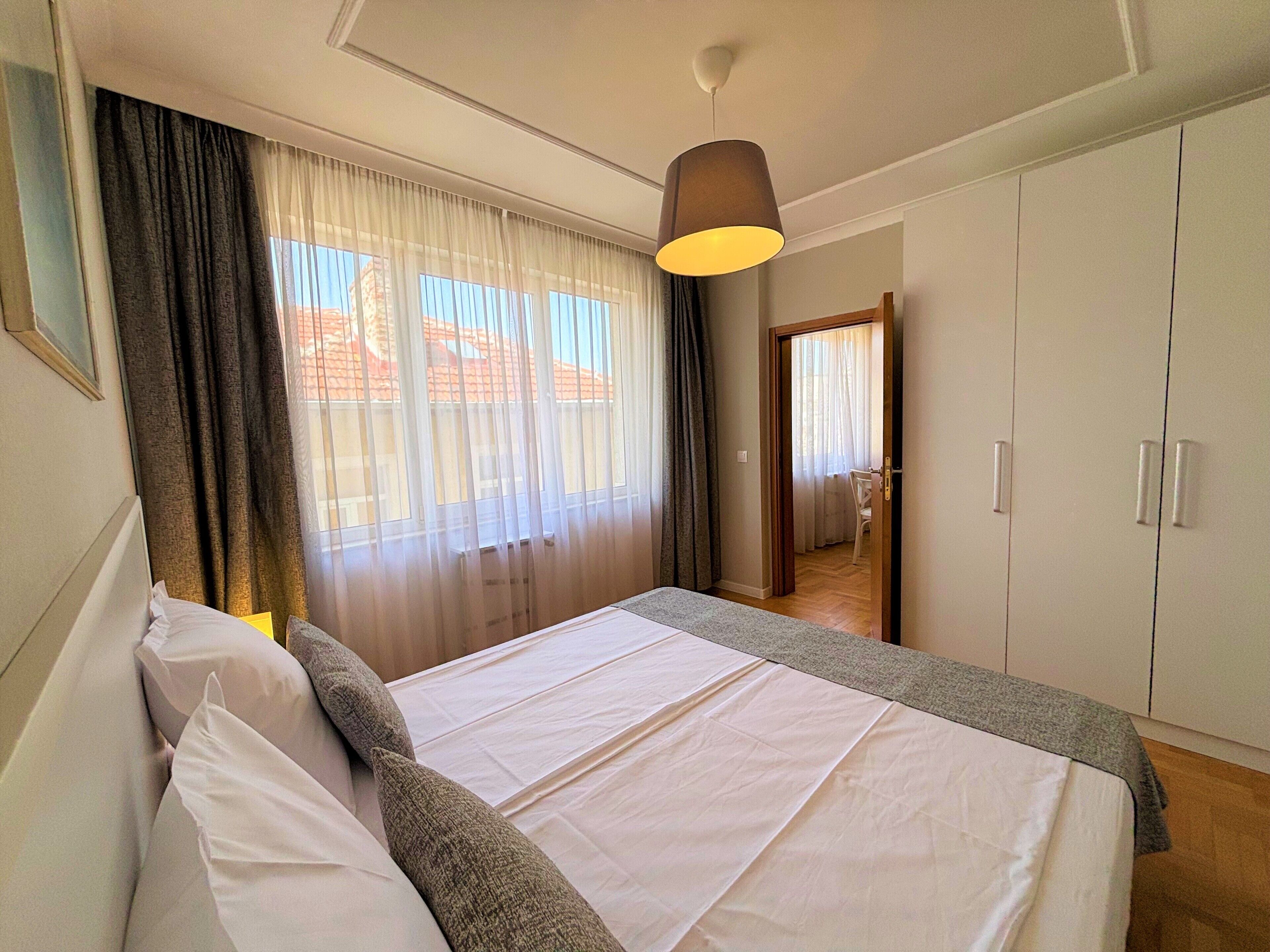 Une chambre à coucher avec un lit, des rideaux, un luminaire suspendu et une armoire.