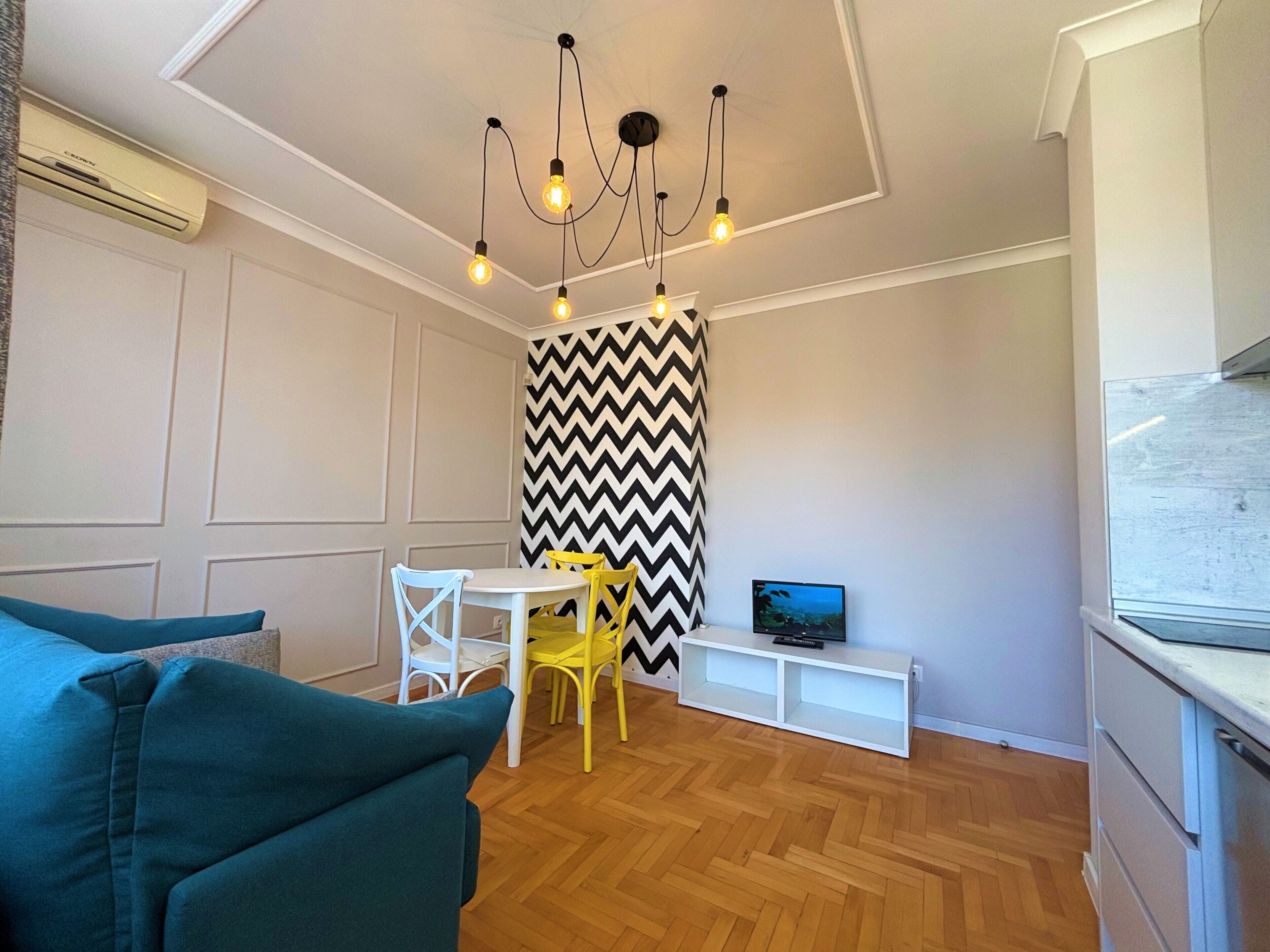 Un espacio habitable compacto con comedor, sofá, televisor e iluminación moderna.