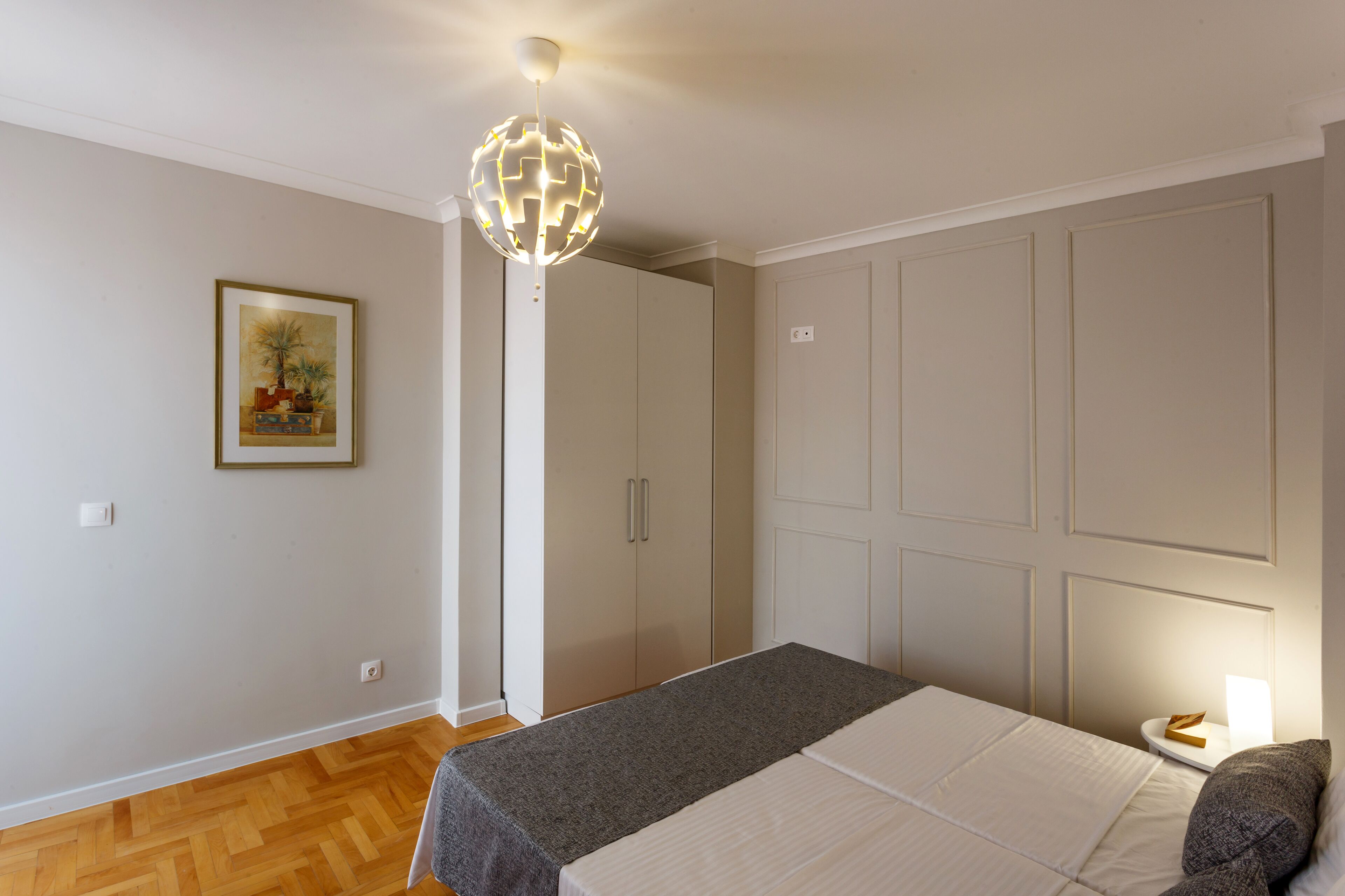 A bedroom with a bed, a nightstand, a wall-mounted globe light, and a framed picture.