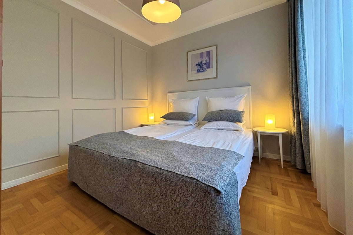 A bedroom with a large bed, two bedside tables, a hanging light fixture, and a framed picture on the wall.