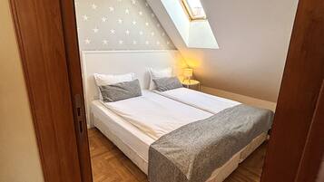 A bedroom with a bed, a nightstand, a lamp, a star-patterned wall, and a sloped ceiling with a skylight.