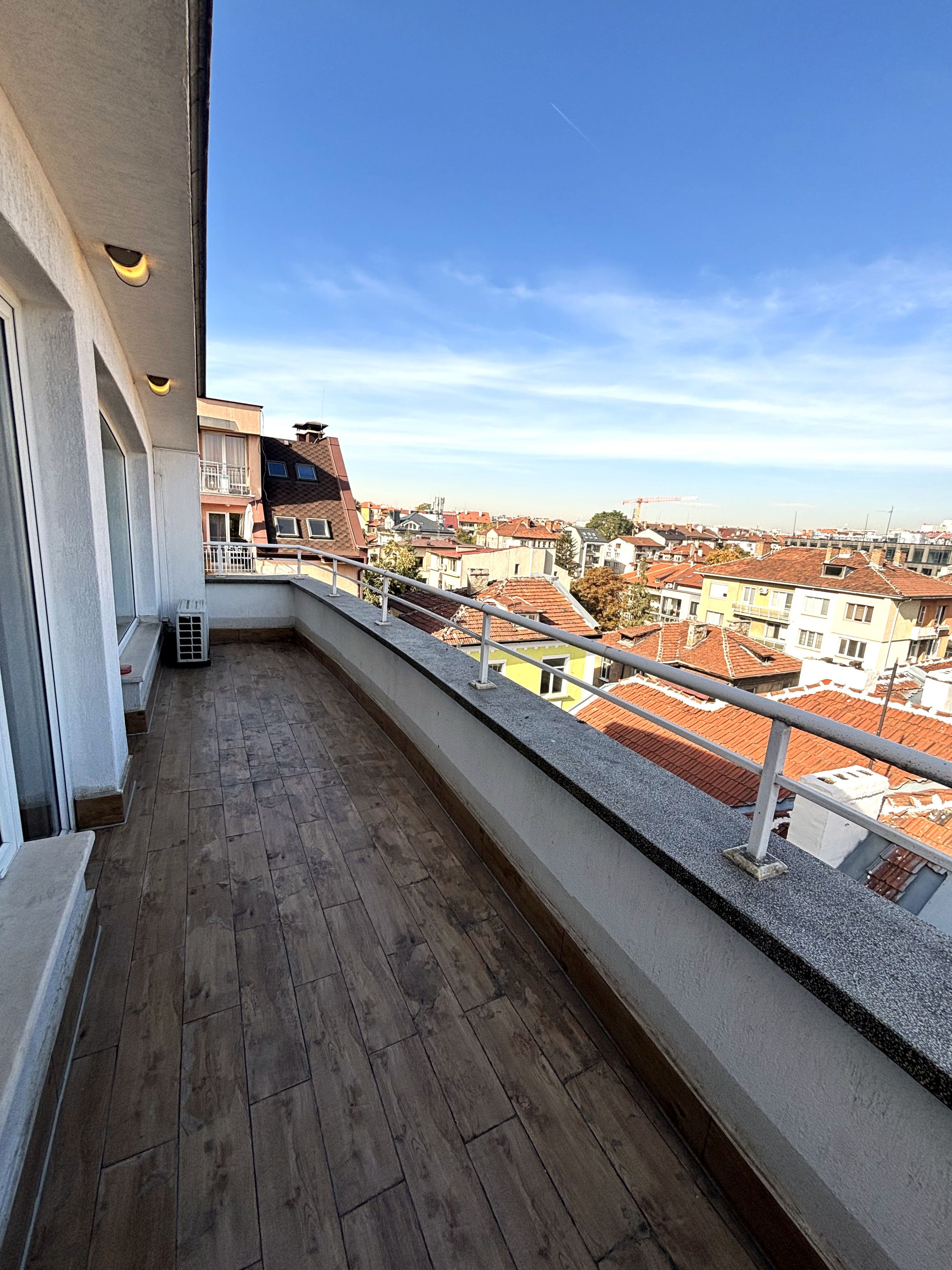 A balcony with a view of a residential area, wooden flooring, and a railing.