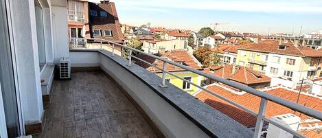 Un balcón con vista a una zona residencial, suelo de madera y barandilla.