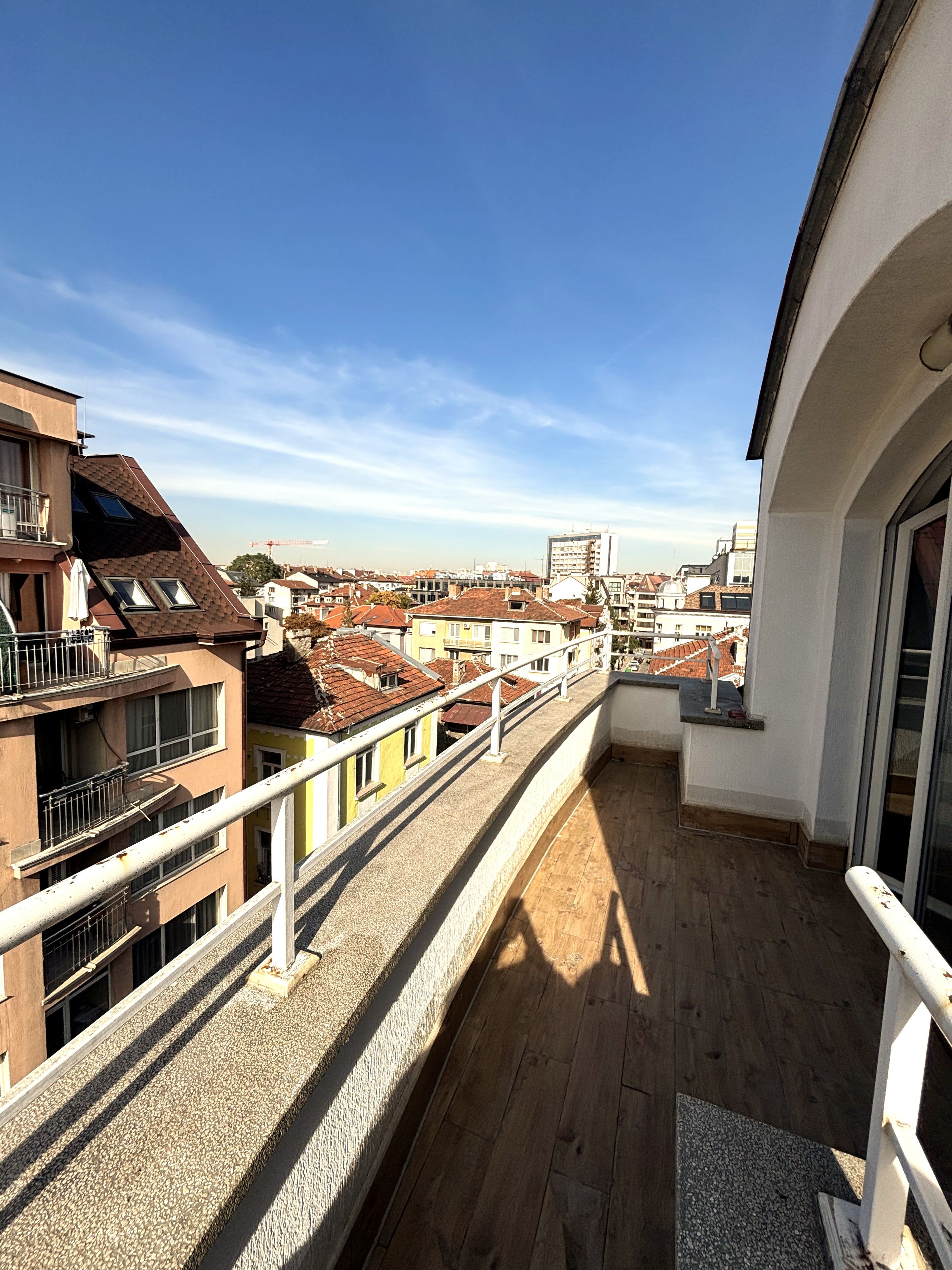 A balcony with a view of a cityscape, featuring buildings with red-tiled roofs and a clear blue sky.