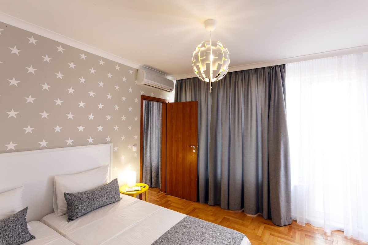 A hotel room with a bed, a nightstand, a lamp, a globe light, a wardrobe, and a window with curtains.