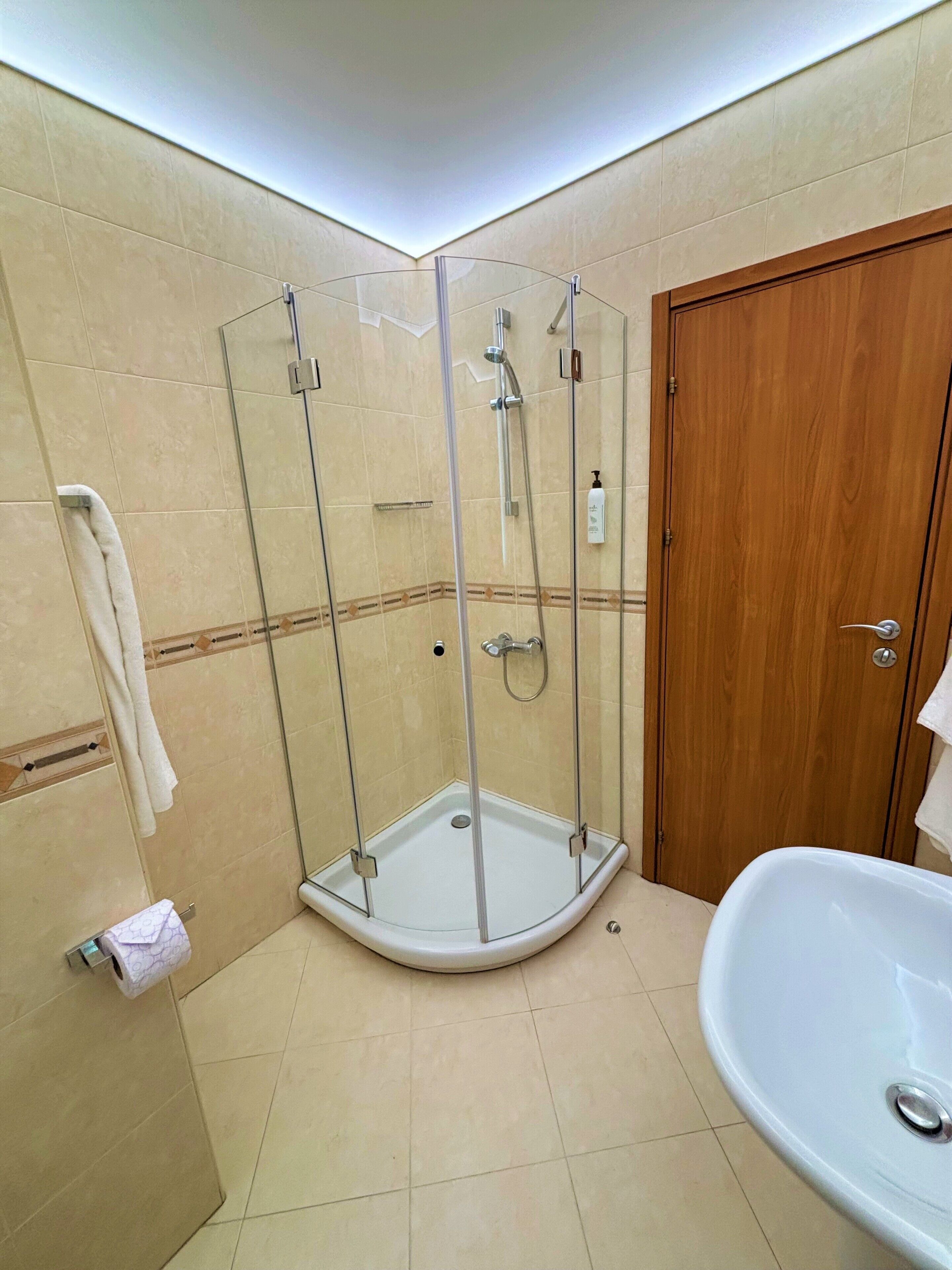A bathroom with a glass-enclosed shower, a wooden door, and a white bathtub.