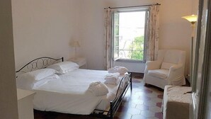 Ein Schlafzimmer mit Bett, Stuhl, Fenster mit Vorhängen und Lampe.