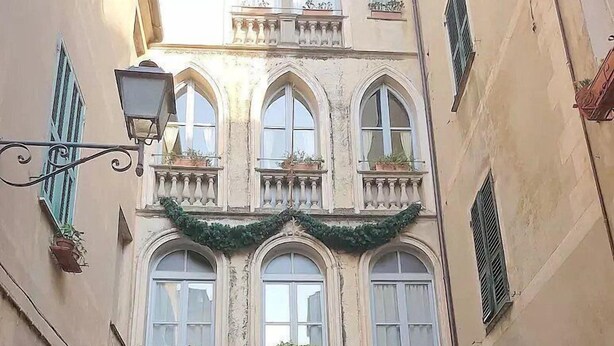 Ein Gebäude mit Bogenfenstern, einem mit Pflanzen bepflanzten Balkon und einer hängenden Girlande.