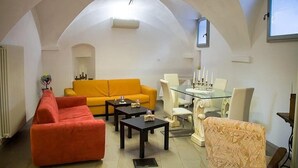 Ein Wohnzimmer mit hoher, gewölbter Decke, einem gelben Sofa, einem roten Sofa, einem Glastisch mit Stühlen und einem Kamin.