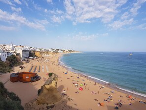 A coastal beach with a rocky outcrop, a wooden building labeled 'ROCA', and a clear sky.