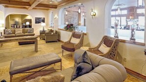 Amplia sala de estar con techos altos, vigas de madera y ventanas grandes. Ofrece múltiples opciones de asiento, incluyendo sofás, sillones y un banco.