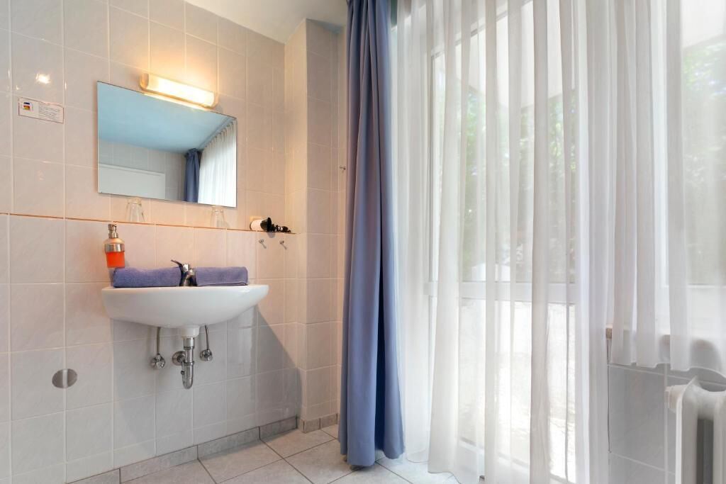 A bathroom with a white sink, mirror, and a window with sheer curtains.