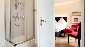 A hotel room with a shower, a bed, a red chair, and a bedside table. - Hotel Helgolandia (Helgoland)