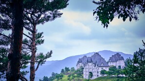 A large, castle-like building with multiple towers, surrounded by lush greenery and a golf course. - Sono Felice Vivaldi Park (Hongcheon)