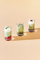 Tres bebidas en capas, servidas en vasos sobre una superficie reflectante.