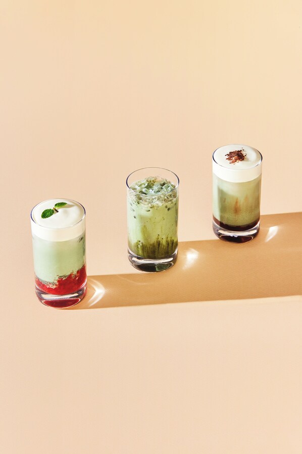 Tres bebidas en capas, servidas en vasos sobre una superficie reflectante.