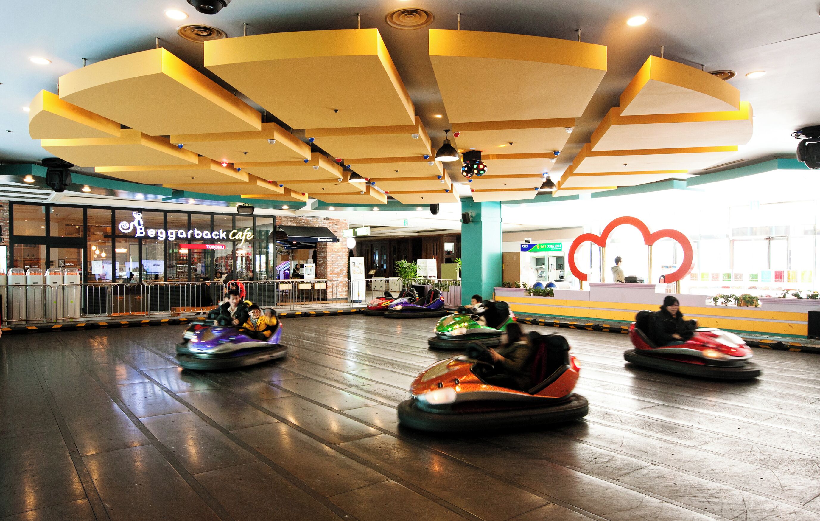 A spacious indoor area with a large open space for bumper cars, a cafe named 'Beggarback Cafe' in the background, and a distinctive red cloud-shaped decoration on the wall.