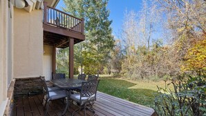A wooden deck with a table and chairs, surrounded by a garden with various plants and trees.