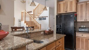 A kitchen with granite countertops, a black refrigerator, wooden cabinets, and a staircase leading to another level.