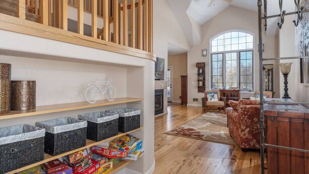 A spacious living room with a wooden staircase, a fireplace, and a large window.