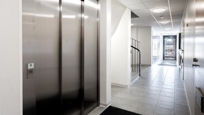 Een moderne hal met een lift, een glazen deur en een betegelde vloer.