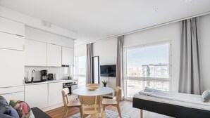 Een moderne, compacte leefruimte met een kitchenette, eethoek en een bed.