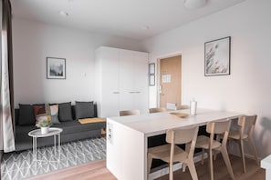 Uma sala de estar moderna com sofá, mesa de jantar e cadeiras. Há uma pequena mesa lateral com uma planta.
