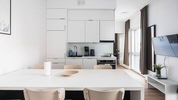 A modern kitchen with white cabinets, a dining table with two chairs, and a large window with curtains.