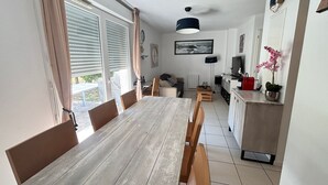 Un comedor con una mesa y sillas de madera, una cocina con armarios y electrodomésticos, y vistas al exterior a través de amplios ventanales.