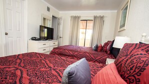 Ein Hotelzimmer mit einem großen Bett, einem Fernseher auf einer Kommode, einem Fenster mit Vorhängen und einem Gemälde an der Wand.