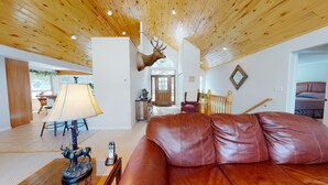 A spacious living room with a leather sofa, a mounted deer head, and a wooden ceiling. - Taylormade Getaway - Almont (Almont)