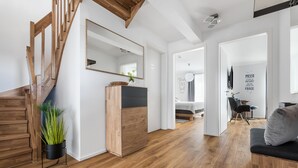Ein modernes Wohnzimmer mit einer Holztreppe, einem spiegelnden Rahmen in Schwarz, einer Holzkabine und einem schwarzen Sofa mit grauem Kissen.