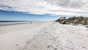A wide sandy beach with footprints leading to the water, a building on a cliff, and a partly cloudy sky. - Ponce Inlet Condo w/ Beach & Pool Access! (Ponce Inlet)