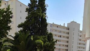 Una piscina con barandilla metálica, rodeada de vegetación y edificios al fondo.