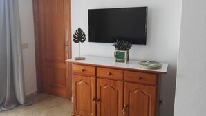 Un mueble de madera con un televisor de pantalla plana montado encima, una planta decorativa y una mesita con un plato.