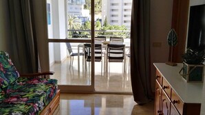 Una sala de estar con un sofá, una mesa de comedor con sillas y un ventanal corredero que da a un balcón exterior.