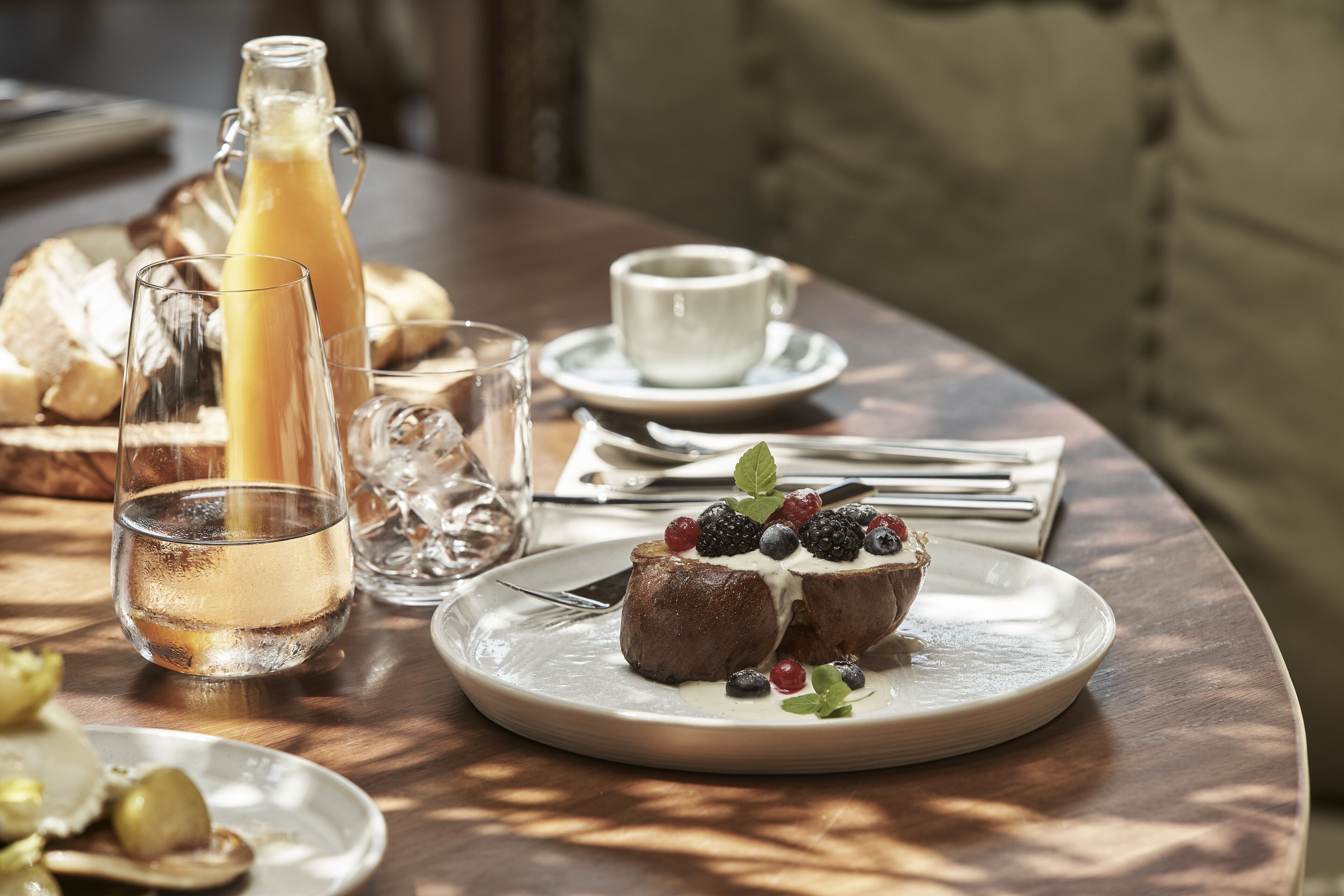 Ein Frühstückstisch mit Speisen, einem Glas Saft und einer Orangenspalte.