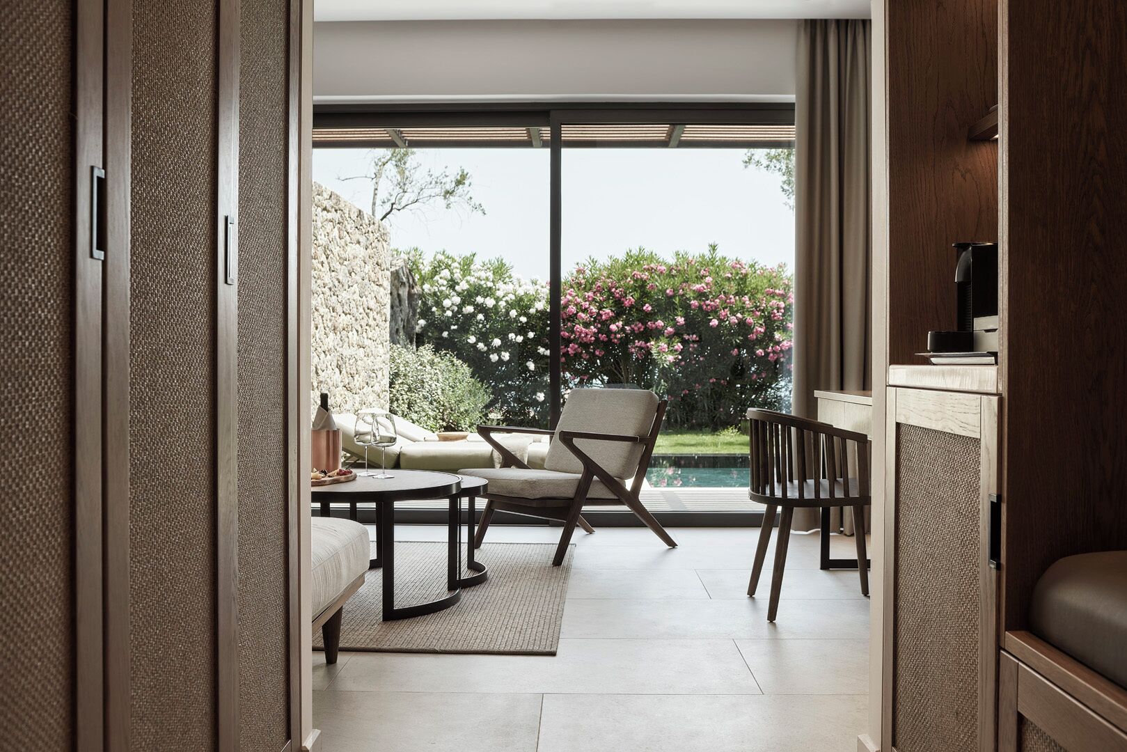 Un interior moderno con sofá, sillón y mesa de comedor cerca de un ventanal con vistas a un jardín.