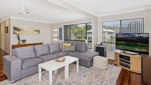 Ein modernes Wohnzimmer mit einem grauen Ecksofa, einem weißen Couchtisch und einem Flachbildfernseher auf einem Holzständer.