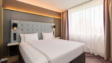 Ein Hotelzimmer mit einem großen Bett, einem Nachttisch, einer Wandleuchte und einem Fenster mit transparenten Vorhängen.