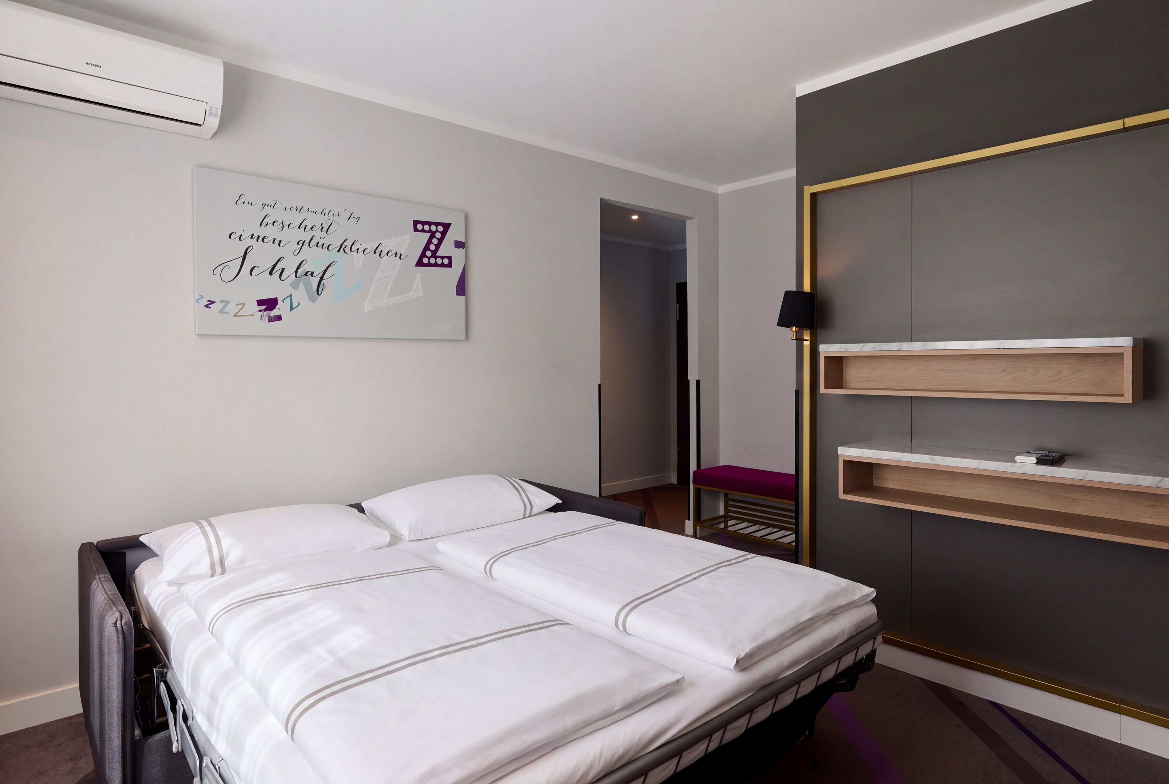 Habitación de hotel con una cama, una mesita de noche, un armario y aire acondicionado instalado en la pared.
