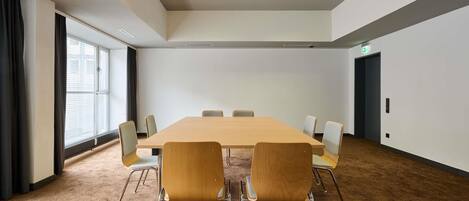 Un salón de conferencias con una mesa larga, seis sillas, suelo alfombrado, luces de techo y una ventana con cortinas.