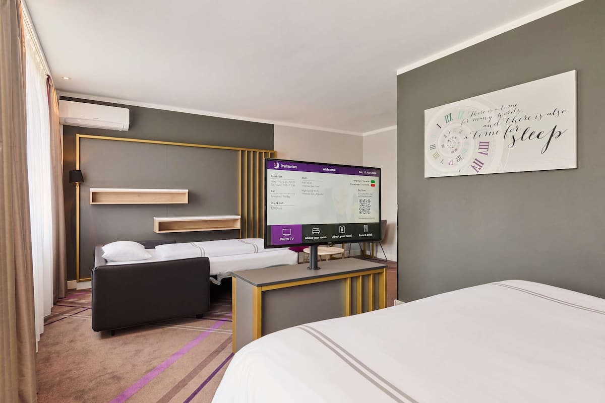 Et hotelværelse med en seng, et skrivebord med computer, et fjernsyn og et vægur.