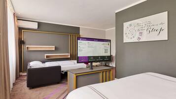 A hotel room with a bed, a desk with a computer, a TV, and a wall clock.