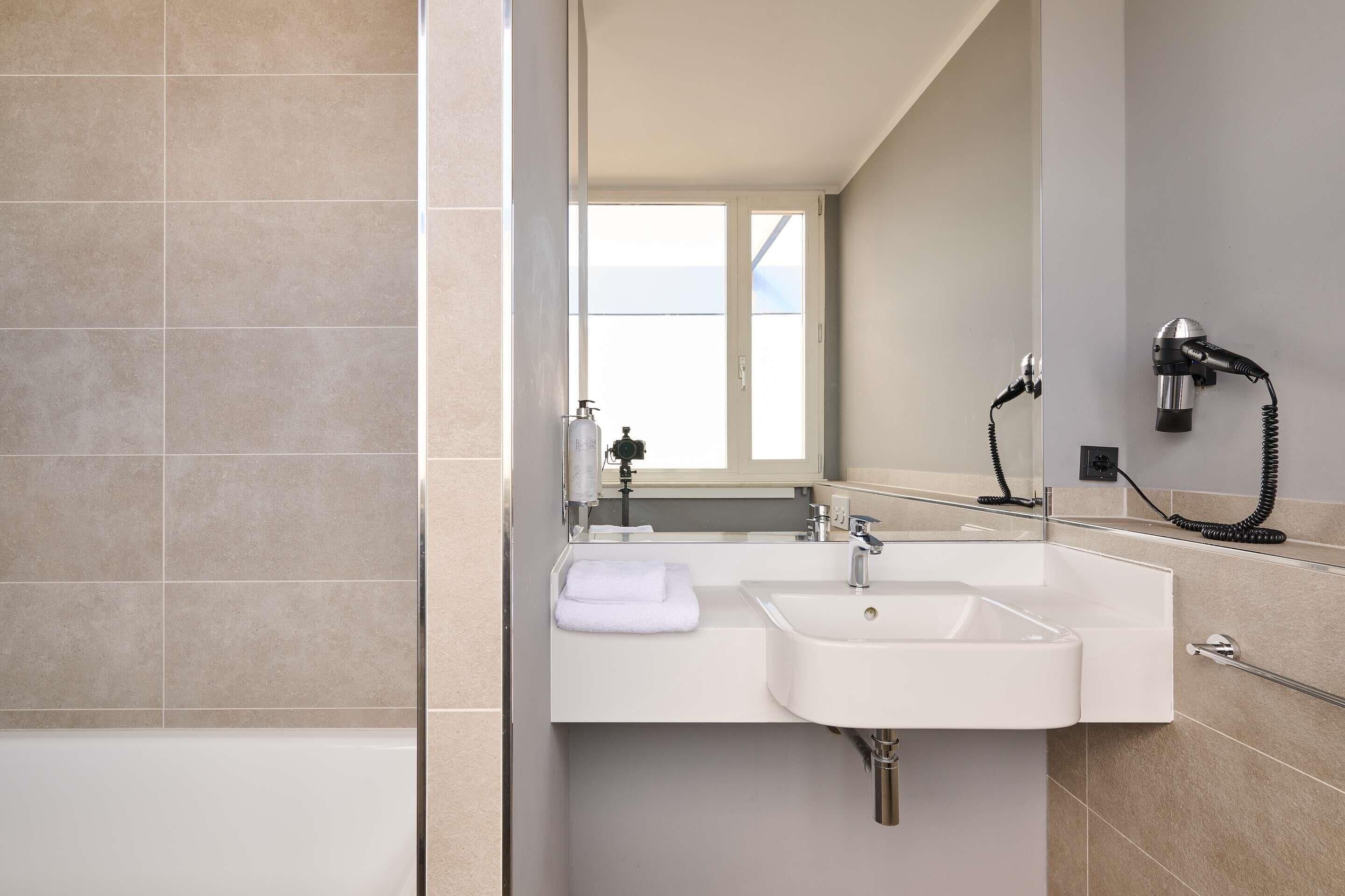 A modern bathroom with a bathtub, two sinks, a towel, and a hairdryer.