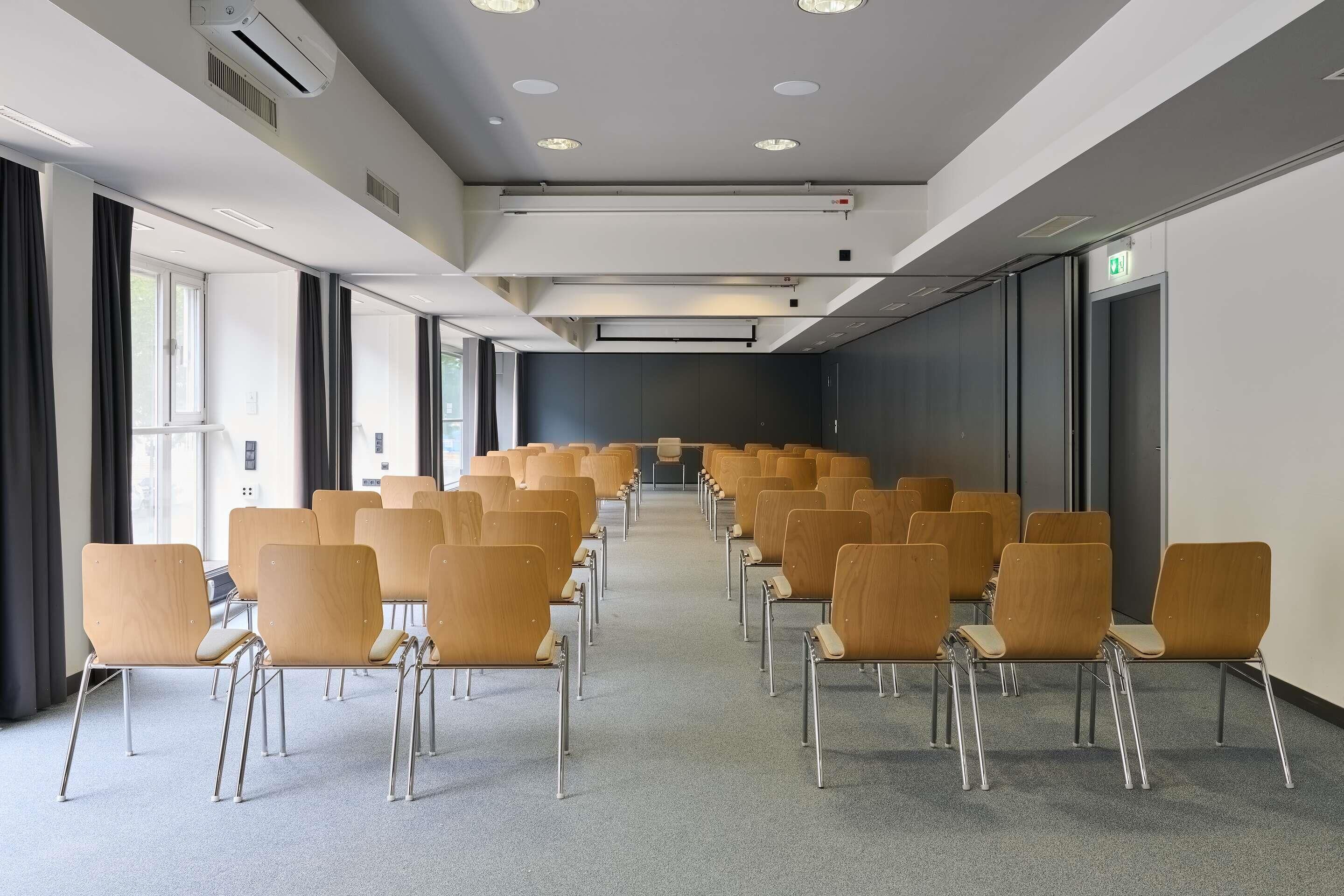 Une salle de conférence avec des rangées de chaises, des unités de climatisation et des fenêtres.