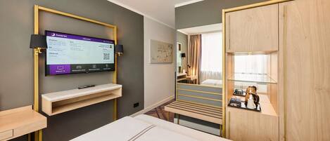 Una habitación de hotel con una cama, un televisor montado en la pared, un escritorio con lámpara y un armario.