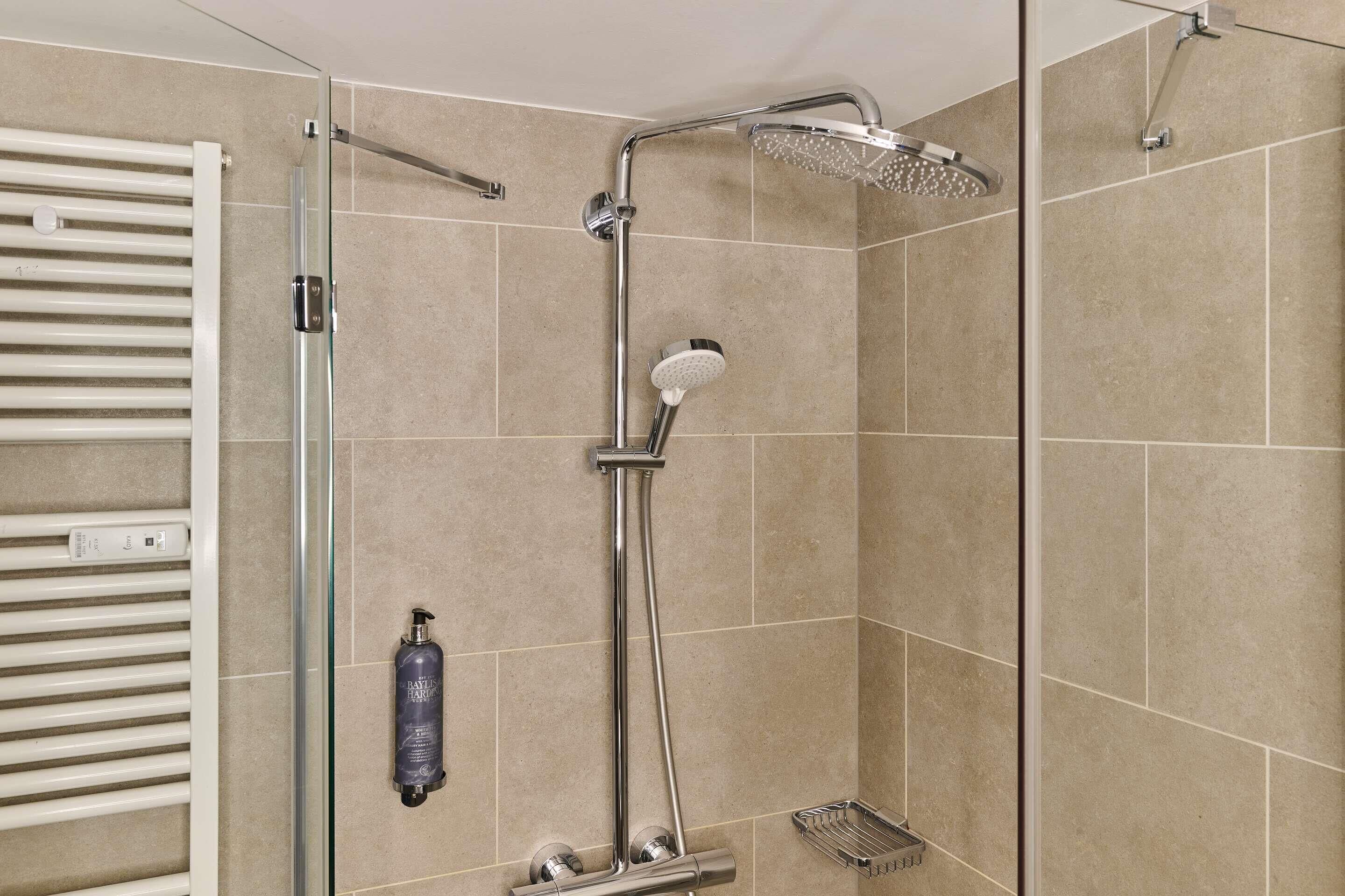 A shower with a handheld showerhead, a wall-mounted faucet, and a handheld showerhead.