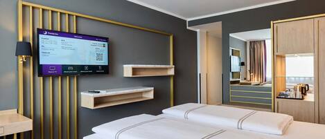 A hotel room with two beds, a TV mounted on the wall, a wooden shelf, and a mirror.