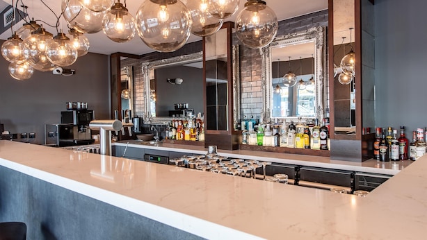 A bar area with a long counter, multiple hanging light fixtures, and a large mirror. - Premier Inn Saarbrücken City Centre (Saarbrucken)